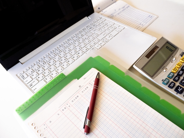 PCや電卓などデスク上に仕事道具が広げられている